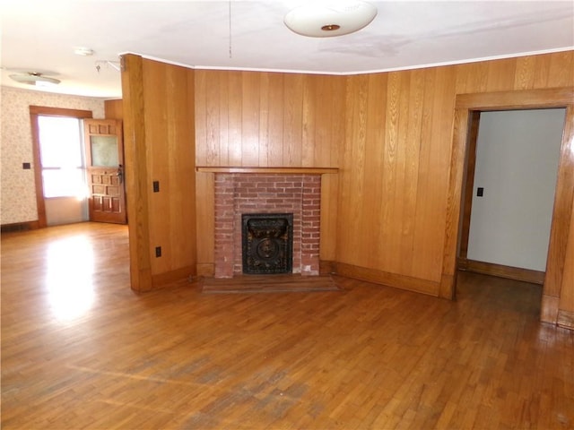 unfurnished living room featuring wooden walls, a fireplace, wood finished floors, baseboards, and ornamental molding