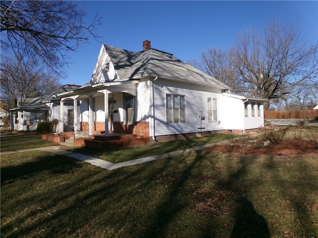 view of side of home featuring a porch, a yard, and a chimney