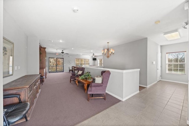 interior space with ceiling fan with notable chandelier, light tile patterned flooring, light colored carpet, and baseboards