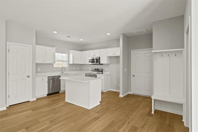 kitchen featuring light wood-style flooring, stainless steel appliances, a sink, white cabinets, and light countertops