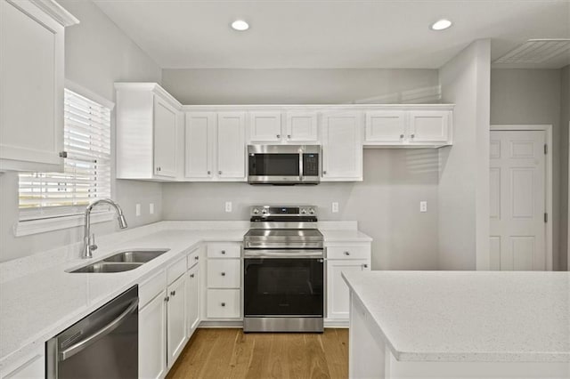 kitchen with white cabinets, appliances with stainless steel finishes, light wood-type flooring, a sink, and recessed lighting