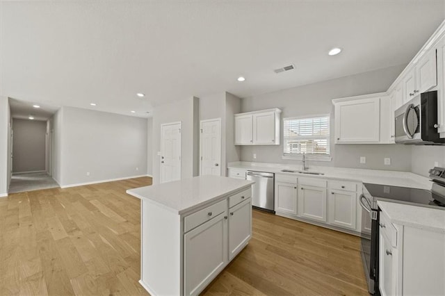 kitchen with light wood finished floors, visible vents, appliances with stainless steel finishes, a sink, and a kitchen island