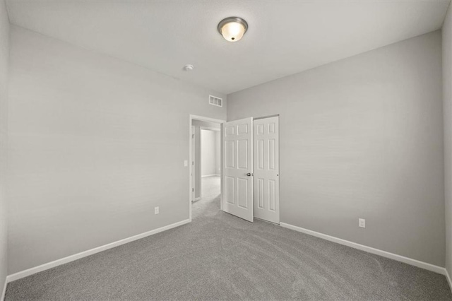 unfurnished room with carpet, visible vents, and baseboards