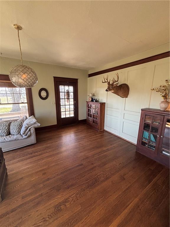 living room with dark wood-type flooring, a decorative wall, and baseboards