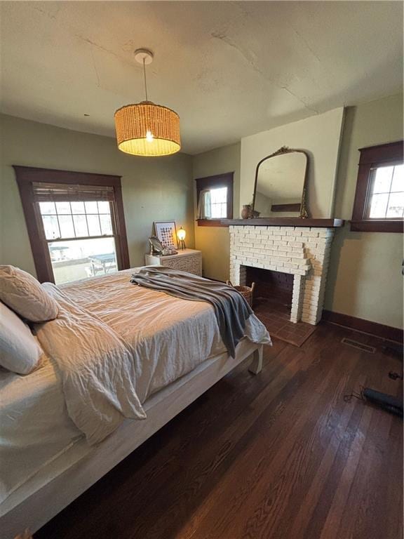 bedroom featuring a brick fireplace, visible vents, baseboards, and wood finished floors