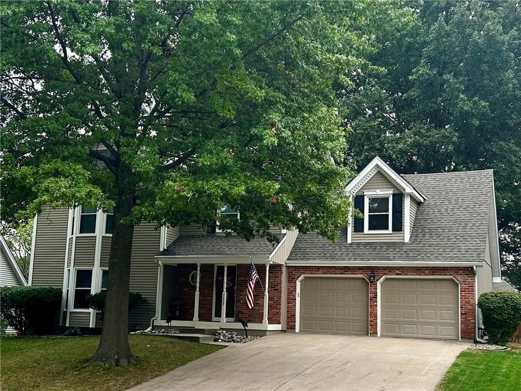 view of front of property featuring a shingled roof, concrete driveway, a front lawn, a garage, and brick siding