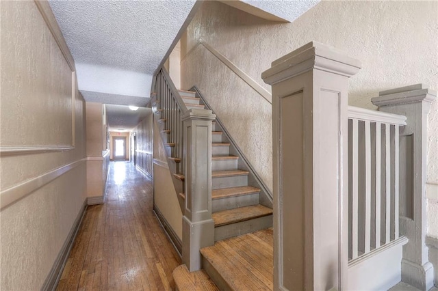 stairway featuring wood-type flooring, baseboards, a textured ceiling, and a textured wall