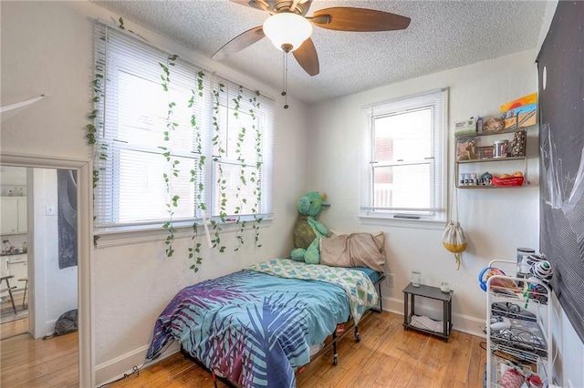 bedroom with baseboards, multiple windows, a textured ceiling, and hardwood / wood-style floors