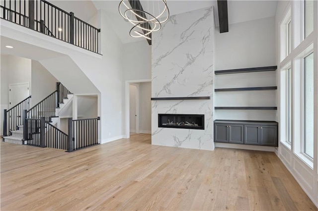 unfurnished living room featuring a chandelier, a fireplace, a towering ceiling, and light wood finished floors