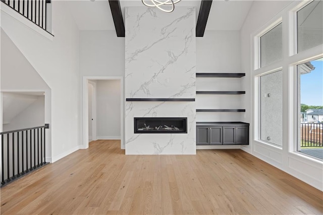 unfurnished living room featuring light wood-style floors, beam ceiling, a high ceiling, and a premium fireplace