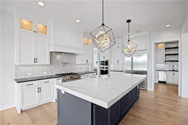 kitchen with built in appliances, a sink, white cabinets, light wood-type flooring, and glass insert cabinets