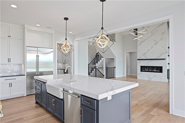 kitchen featuring light wood-style flooring, stainless steel appliances, a fireplace, white cabinetry, and a sink