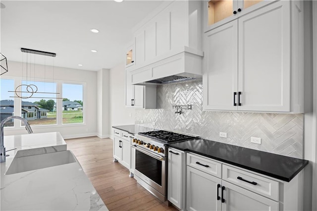 kitchen featuring high end stove, white cabinetry, and a sink