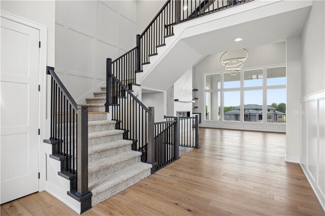 staircase with a high ceiling, a fireplace, a decorative wall, and wood finished floors