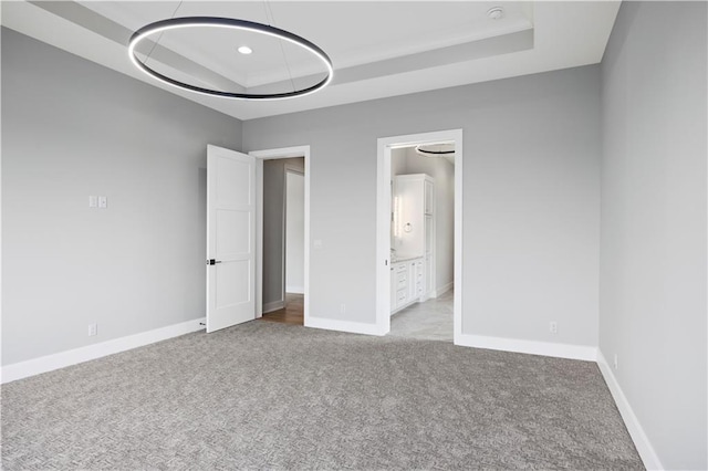 unfurnished bedroom featuring carpet, a raised ceiling, and baseboards