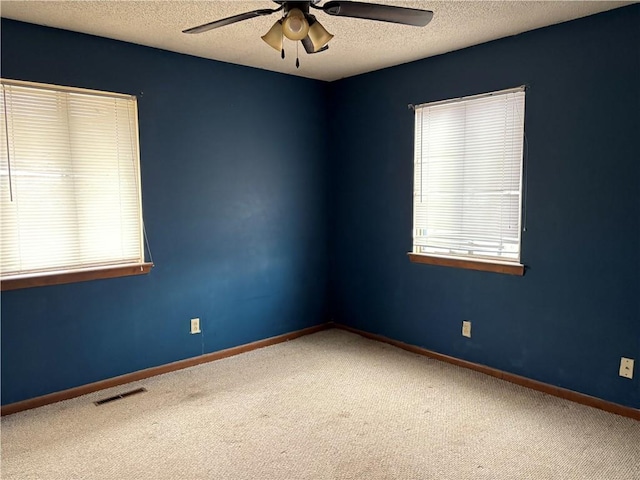 empty room with carpet, visible vents, ceiling fan, a textured ceiling, and baseboards