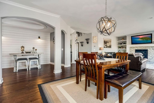 dining room with wood finished floors, ornate columns, arched walkways, a glass covered fireplace, and crown molding