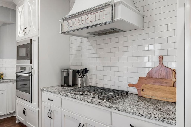 kitchen with light stone countertops, stainless steel appliances, white cabinets, exhaust hood, and backsplash