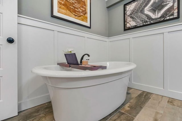 full bath with a freestanding tub, wood finished floors, and a decorative wall