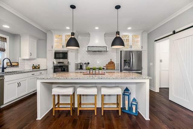 kitchen with custom range hood, ornamental molding, a barn door, stainless steel appliances, and a sink