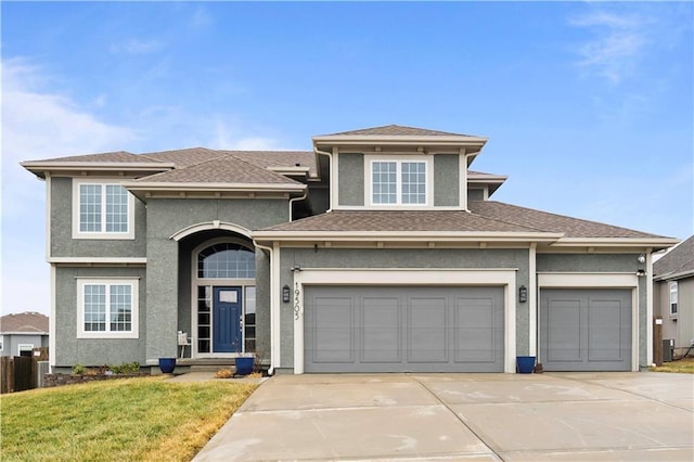 view of front facade with concrete driveway, a shingled roof, a front yard, and stucco siding