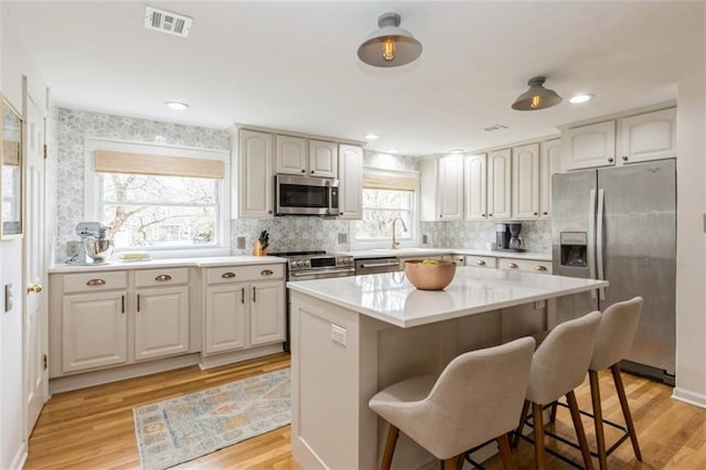 kitchen with visible vents, appliances with stainless steel finishes, light wood-type flooring, and a kitchen breakfast bar