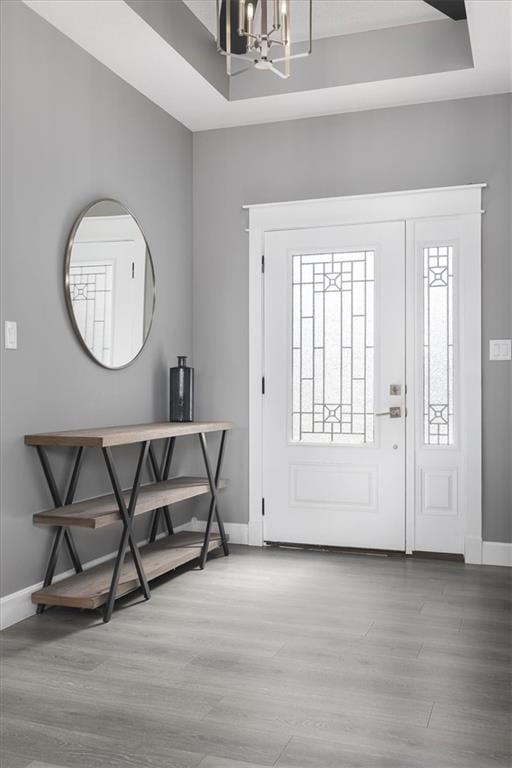 foyer featuring a chandelier, a raised ceiling, baseboards, and wood finished floors