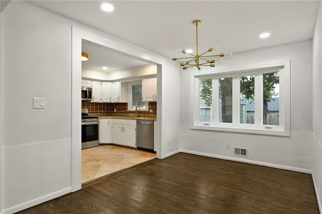 kitchen with visible vents, appliances with stainless steel finishes, light wood-type flooring, white cabinetry, and backsplash