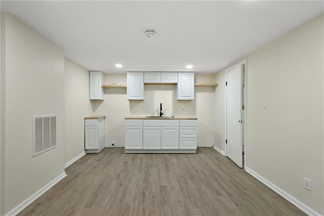 kitchen with light wood finished floors, visible vents, baseboards, white cabinetry, and a sink