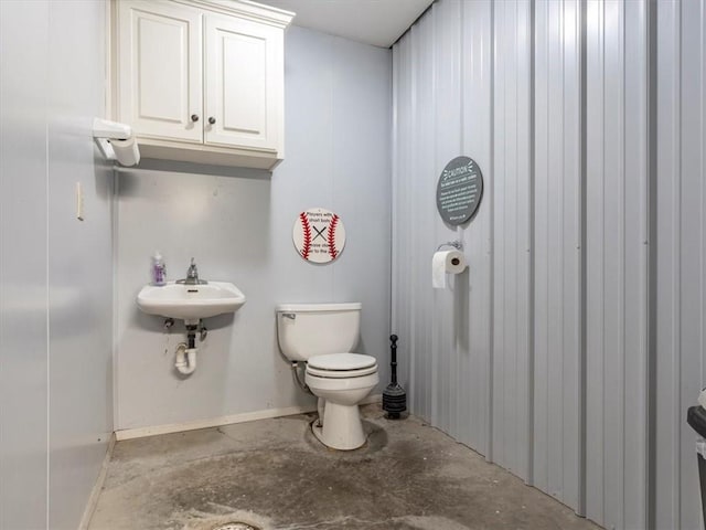 half bath featuring toilet, concrete floors, and a sink