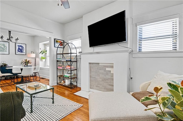 living area featuring a fireplace with flush hearth, baseboards, light wood finished floors, and ceiling fan