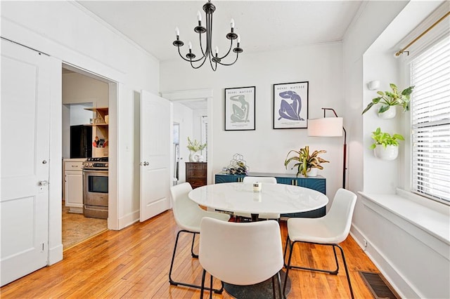 dining space with baseboards, visible vents, light wood finished floors, crown molding, and a chandelier