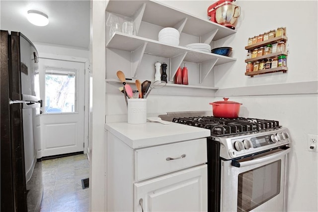 kitchen with stainless steel gas stove, white cabinets, freestanding refrigerator, and open shelves