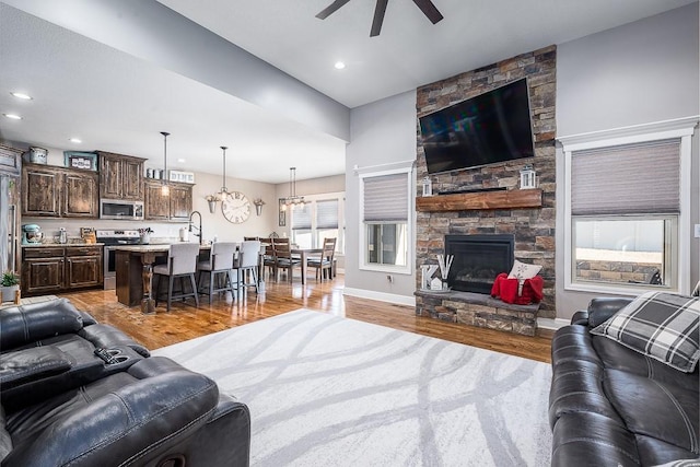 living room with light wood-style flooring, recessed lighting, ceiling fan with notable chandelier, a fireplace, and baseboards