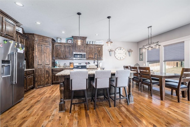 kitchen with dark brown cabinetry, a breakfast bar, light wood-style floors, appliances with stainless steel finishes, and pendant lighting