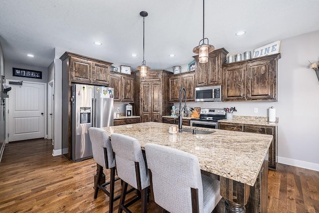 kitchen featuring appliances with stainless steel finishes, dark wood-style flooring, dark brown cabinetry, and light stone counters