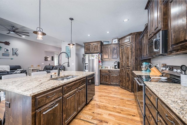 kitchen featuring a sink, open floor plan, appliances with stainless steel finishes, light wood finished floors, and an island with sink