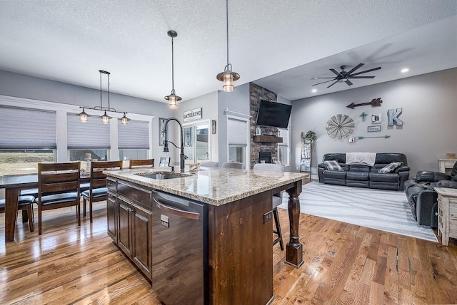 kitchen featuring a stone fireplace, light wood-style flooring, a sink, a kitchen breakfast bar, and stainless steel dishwasher