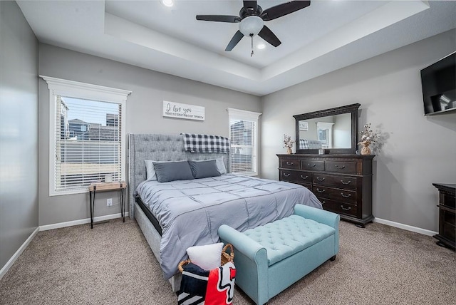 carpeted bedroom with multiple windows, baseboards, and a raised ceiling