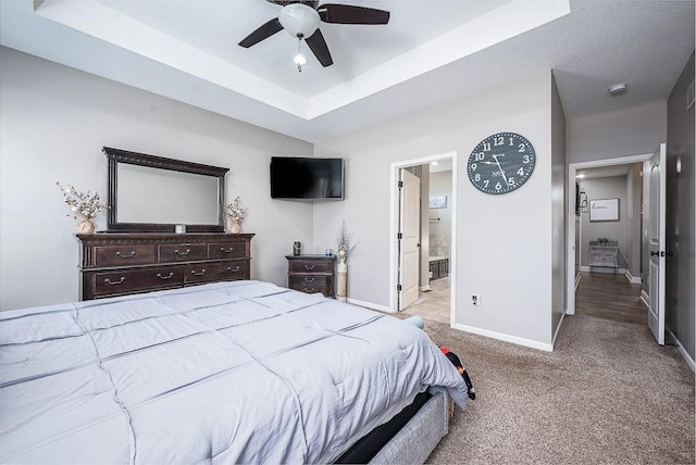 bedroom featuring carpet, a raised ceiling, connected bathroom, ceiling fan, and baseboards