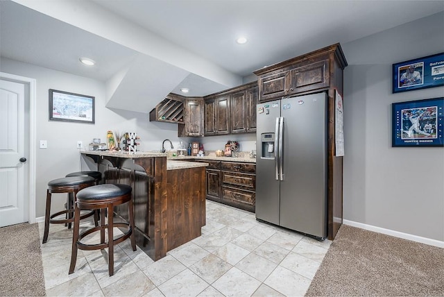 kitchen with dark brown cabinetry, a peninsula, baseboards, a kitchen breakfast bar, and stainless steel fridge