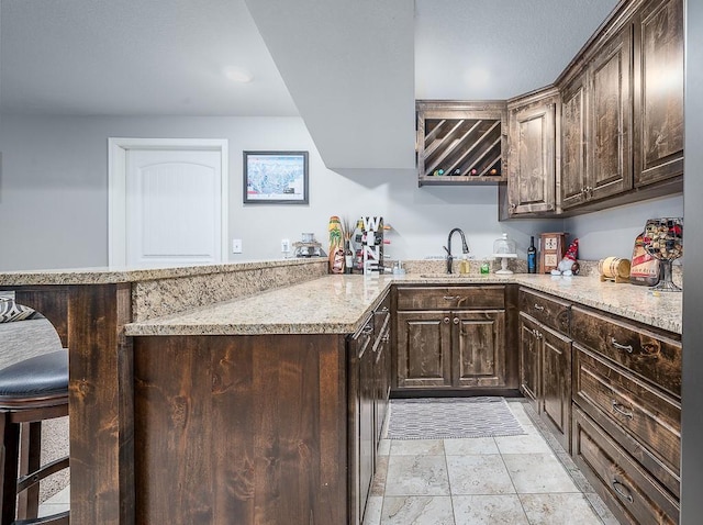 kitchen featuring a peninsula, dark brown cabinetry, light stone counters, and a sink