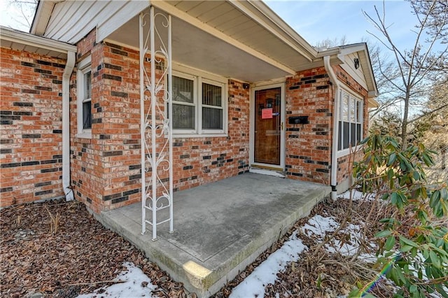 entrance to property featuring crawl space, brick siding, and covered porch