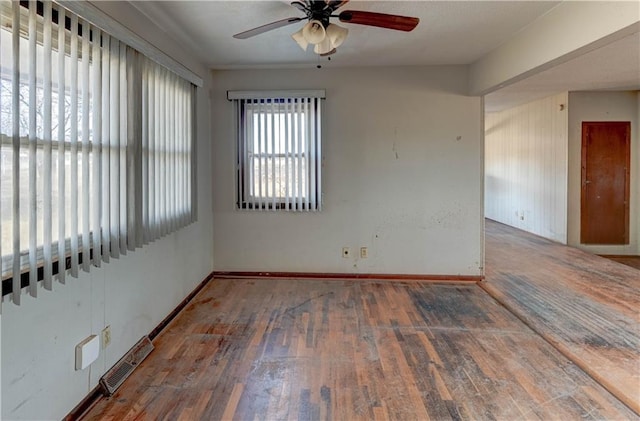 empty room featuring hardwood / wood-style flooring, baseboards, visible vents, and ceiling fan