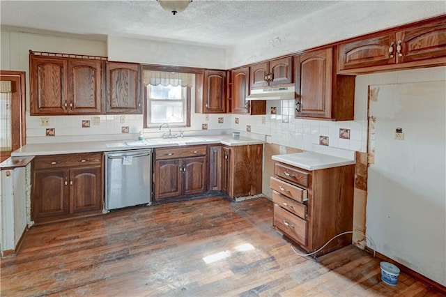 kitchen with tasteful backsplash, under cabinet range hood, dark wood-style flooring, stainless steel dishwasher, and a sink