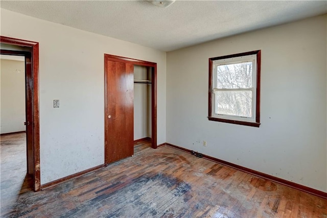 unfurnished bedroom with a closet, a textured ceiling, baseboards, and hardwood / wood-style floors