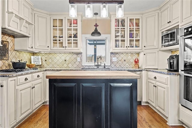 kitchen with a kitchen island, a sink, stainless steel appliances, custom range hood, and light wood-style floors