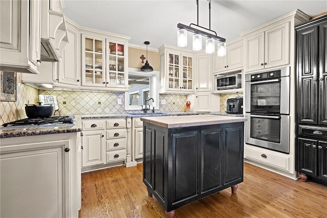 kitchen with a sink, stainless steel appliances, decorative light fixtures, dark cabinets, and a center island