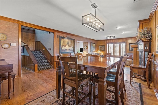 dining area with stairway, wood walls, ornamental molding, an inviting chandelier, and light wood-style floors