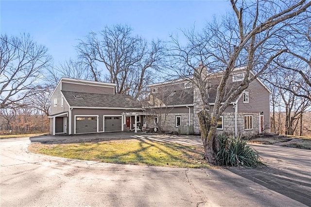 view of front of house with a front yard, driveway, a chimney, a garage, and stone siding